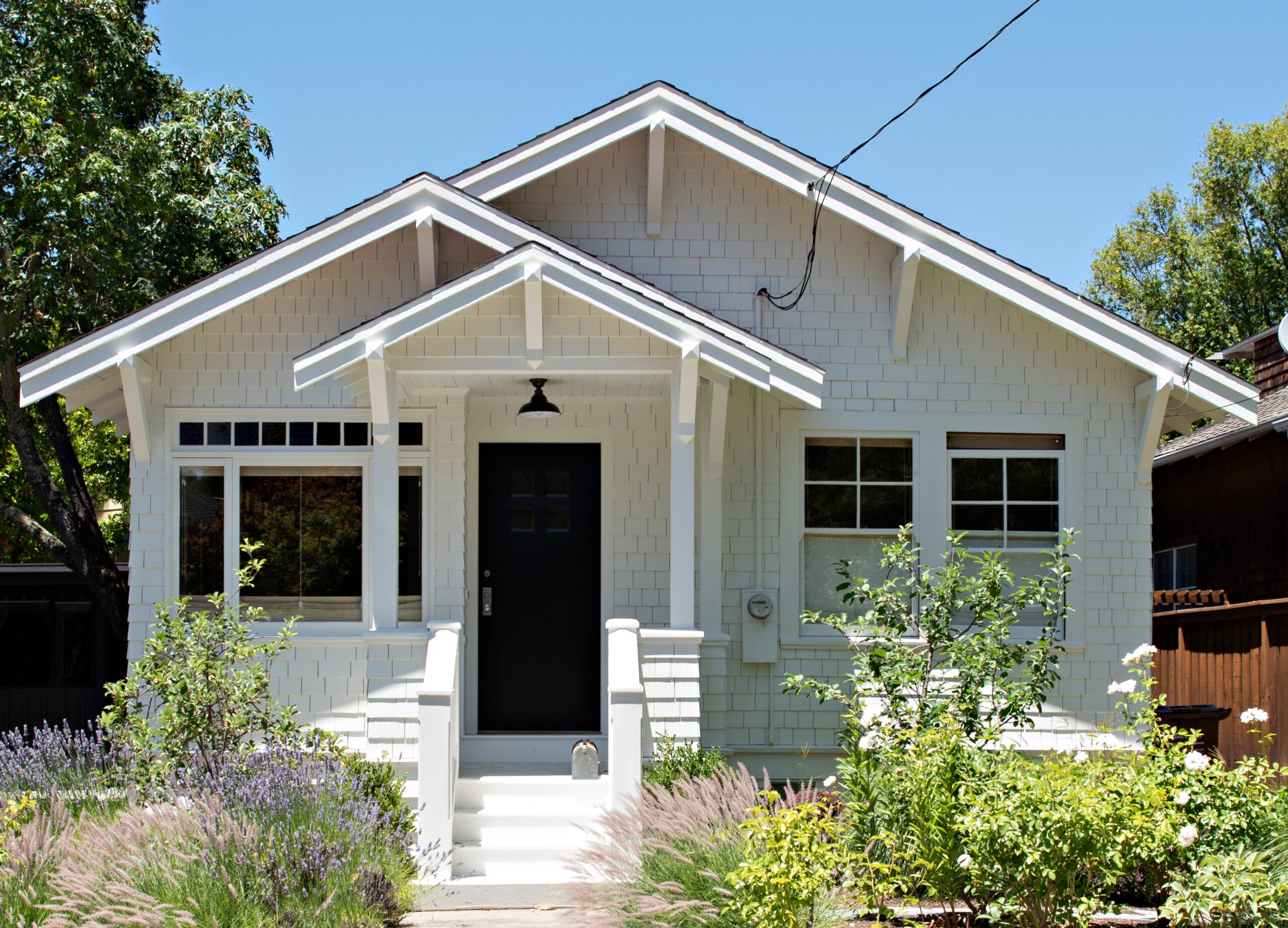 Exterior front porch of an ADU in Summerland, CA, with shingle siding, multiple gables, a black front door, and a black gooseneck pendant light.